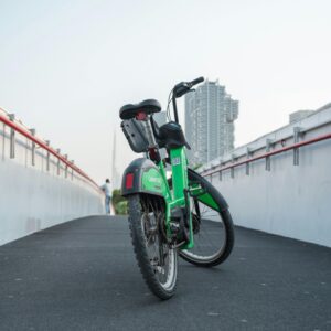 A green bike parked on a city pathway with an urban skyline in the background, offering a modern travel vibe.