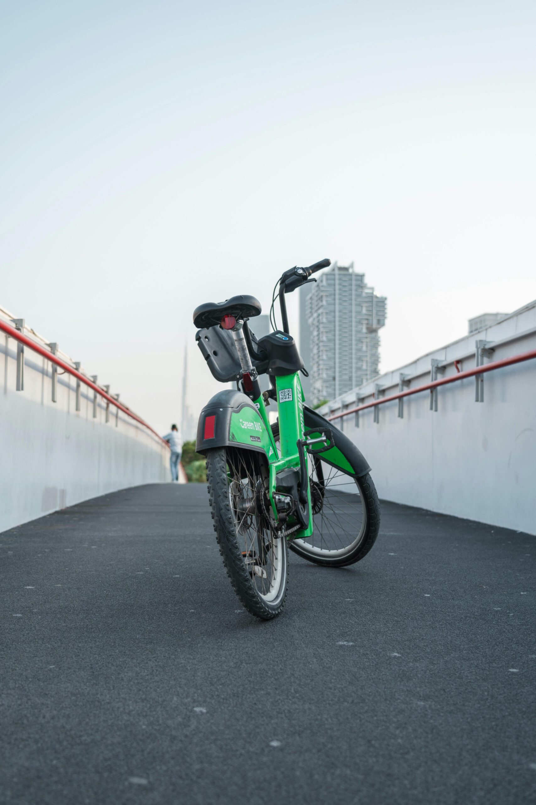 A green bike parked on a city pathway with an urban skyline in the background, offering a modern travel vibe.