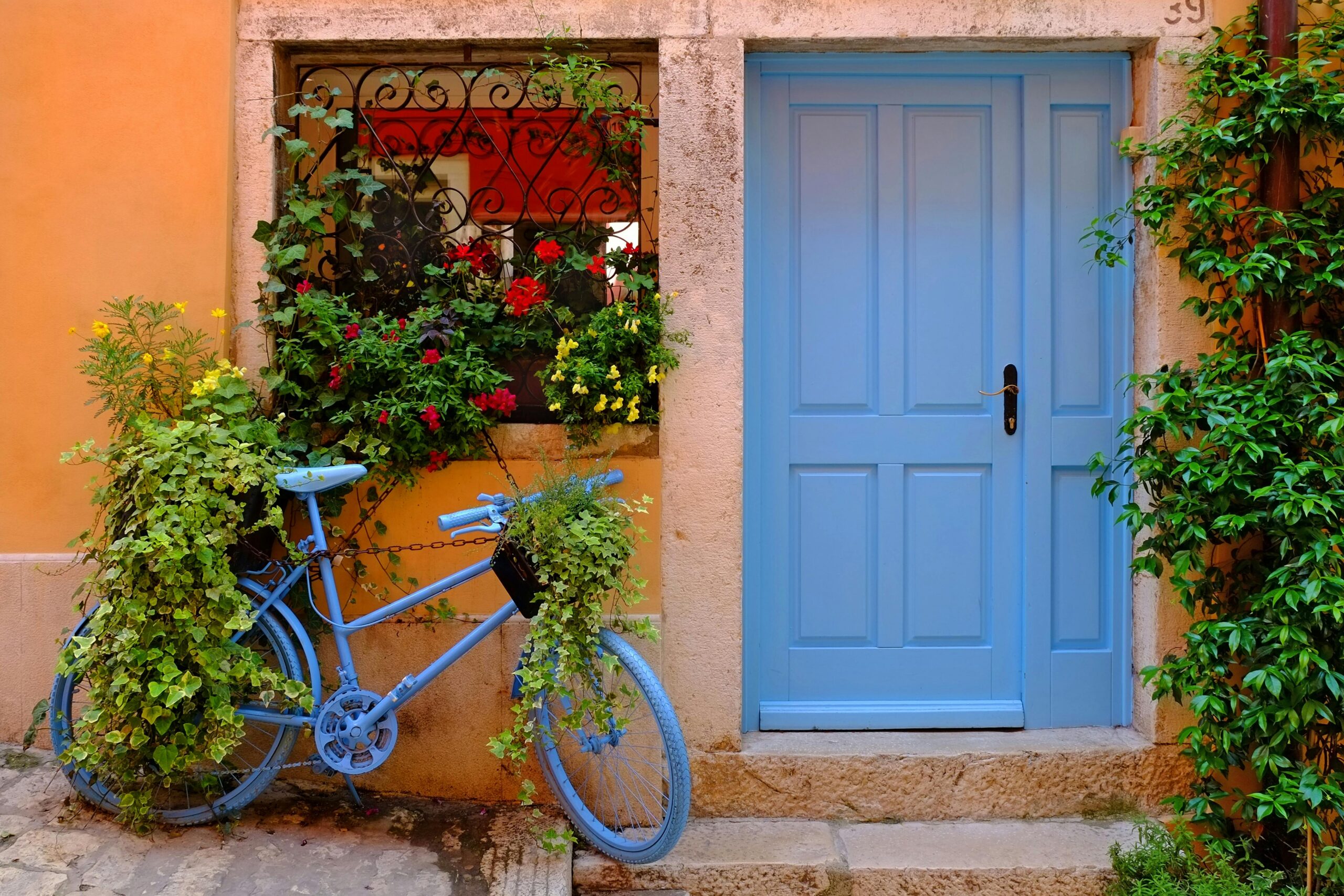 Vibrant blue bicycle against a colorful urban wall adorned with lush flowers and plants.