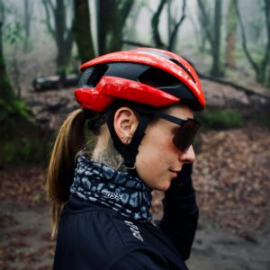 A woman in a red helmet cycling through a misty forest, blending adventure and serenity.