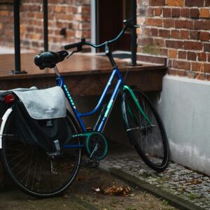 A blue bicycle with panniers rests against a brick wall in an urban setting.