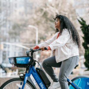Side view of positive African American lady wearing casual clothes while riding bike in town in park in sunny day near buildings and trees